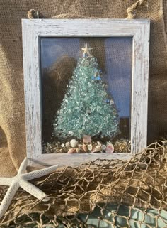 a christmas tree in a frame with shells and starfish on the table next to it