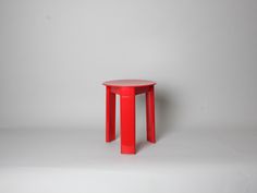 a small red table sitting on top of a white floor next to a gray wall