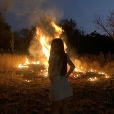 a girl standing in front of a fire with her hands on her hips