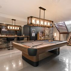 a pool table in the middle of a room with stairs leading up to an upper level