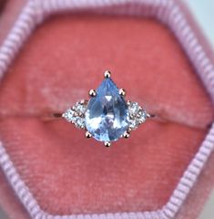 an oval cut blue topaz ring in a pink velvet box with three diamonds around it