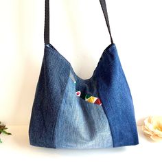 a purse made out of jeans and fabric with buttons on the front, sitting next to a flower