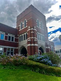 a large brick building with many windows on it's side and flowers in the foreground