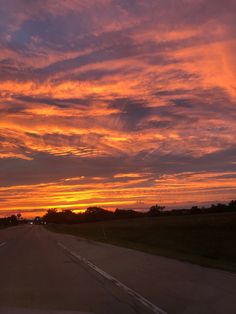 the sun is setting on an empty road with trees in the distance and clouds in the sky