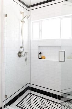 a black and white tiled bathroom with glass shower door, shelves on the wall, and tile floor