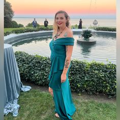 a woman standing in front of a fountain wearing a green dress and holding a necklace