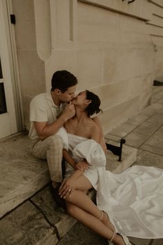 a man and woman sitting on the ground kissing each other while they are dressed in white