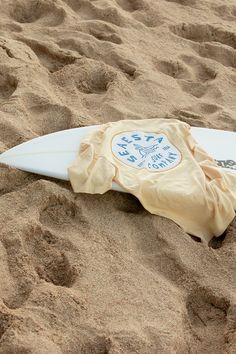 a white surfboard laying in the sand with a yellow cover on it's side