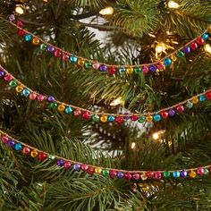 christmas lights are hanging from the branches of a pine tree, which is decorated with multi - colored beads