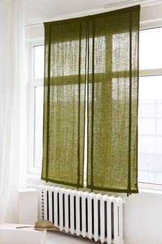 a green curtain hanging over a radiator next to a window with white curtains