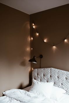 a bed with white sheets and lights hanging from the wall above it in a bedroom