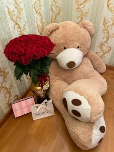 a large teddy bear sitting on top of a wooden floor next to a vase filled with red roses