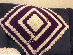 a purple and white crocheted afghan sitting on top of a gray couch next to a wall