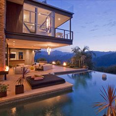 an outdoor living area with fireplaces and couches next to a swimming pool at dusk