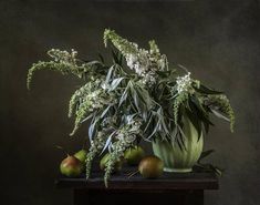 a green vase filled with flowers and fruit on top of a wooden table in front of a dark background