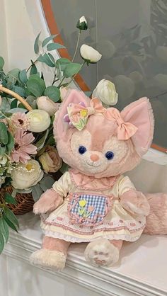 a pink teddy bear sitting on top of a mantle next to a bouquet of flowers