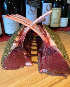 two pieces of raw meat on a cutting board with wine bottles in the back ground