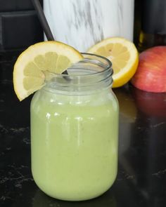 a glass jar filled with green liquid next to sliced lemons and an apple on the side