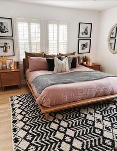 a bed with pink sheets and pillows in a bedroom next to two framed pictures on the wall