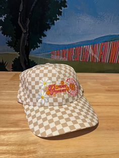 Upgrade your spring and summer style with our Flower Power Checked Cap. This white and tan checkered baseball cap features floral and heart patches for a playful yet stylish look. Get ready to rock your flower power vibes with this quirky and fun accessory! A Cactus Jane Original, made in house at our Laguna Beach store front Sunflower Race Hat, Summer Retro Baseball Cap, Retro Spring Baseball Cap With Curved Brim, Retro Curved Brim Baseball Cap For Spring, Retro Trucker Hat With Curved Visor, Vintage White Baseball Cap For Summer, Spring Cotton Snapback Trucker Hat, Retro White Cotton Trucker Hat, Trendy Snapback Baseball Cap For Spring