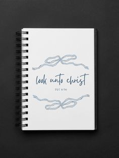 a spiral notebook with the words look at christ written in blue ink on top of it