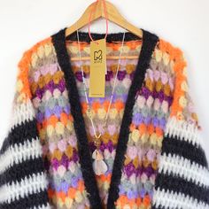 a multicolored cardigan sweater hanging on a wooden hanger with a tag