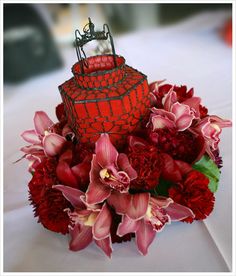 a red vase filled with lots of flowers on top of a white cloth covered table