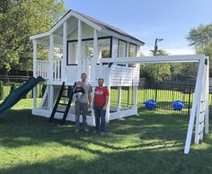 two men standing in front of a white play house with a slide and climbing frame