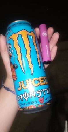 a person holding up a can of monster energy drink with a pink battery in it