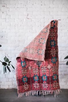 a red and blue blanket sitting on top of a wooden floor next to a white brick wall