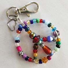 "Groovy gift for that free spirited friend or relative! Each bright and colorful Beaded Wire Peace Sign Keychain is an original, unique and one of a kind. Made from sturdy, tarnish resistant wire, using only quality beads and adorned with a .25\" alloy steel heart charm. Swivel base and lobster claw opening for easy clip on and off. Because no two are alike your item will differ from what is pictured." Word Keychain Beads, Easy Bead Crafts For Adults, Gifts For Hippie Friends, Glass Bead Keychain Diy, Tiny Bead Crafts, Keychain Ideas Diy Beads, Beaded Gifts Diy, Diy Beaded Charms, Brad Keychain