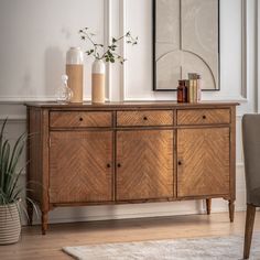 a wooden dresser with two vases on top of it and a plant in the corner