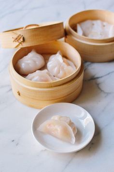 two wooden containers filled with dumplings on top of a white counter next to a plate