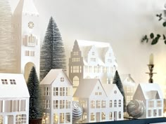 there are many small white houses on the shelf in front of the christmas tree and other decorations