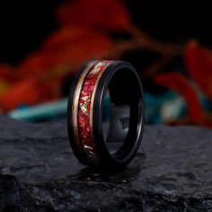 a wedding ring with red and gold inlays on top of a black rock