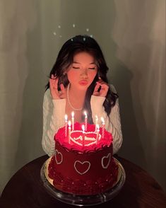 a woman sitting in front of a red cake with candles on it and her hands behind her head