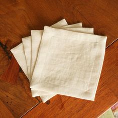 four white linen napkins sitting on top of a wooden table next to a rug