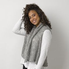 a smiling woman wearing a gray scarf and black leggings, standing in front of a white wall