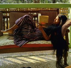 a woman sitting on a bench reading a book with her legs crossed and long hair in the air