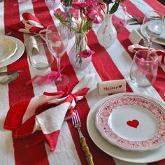 a red and white striped table cloth with pink flowers in vases, plates and utensils