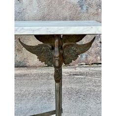 a marble topped table with angel wings on it's legs, against a stone wall