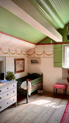 an old fashioned bedroom with green and red accents on the walls, wood flooring and white furniture