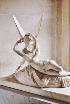 a statue of a woman laying on top of a marble bench with wings flying above her head