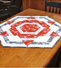 a wooden table topped with a red and white quilted placemat on top of a wooden table