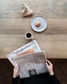 a person sitting at a table reading a newspaper with a cup of coffee next to it