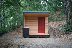 a small wooden outhouse in the woods with red door and steps leading up to it