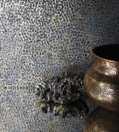 a vase with some black stuff next to it on the ground and a wall covered in mosaic tiles