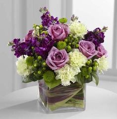 a square vase filled with purple and white flowers