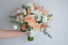 a bridal bouquet is being held by someone's hand against a white wall