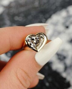 someone is holding a heart shaped diamond ring in their left hand and it's on the tip of her finger